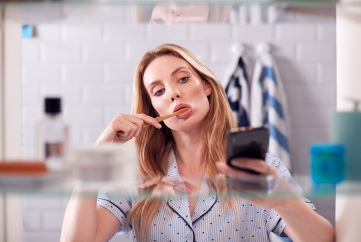 Woman-brushing-teeth-looking-at-phone