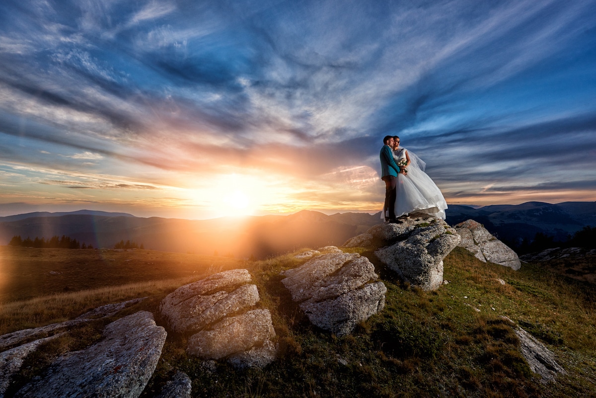 get married somewhere breathtaking Just married couple standing on rocks with the sun setting over the mountains in the background